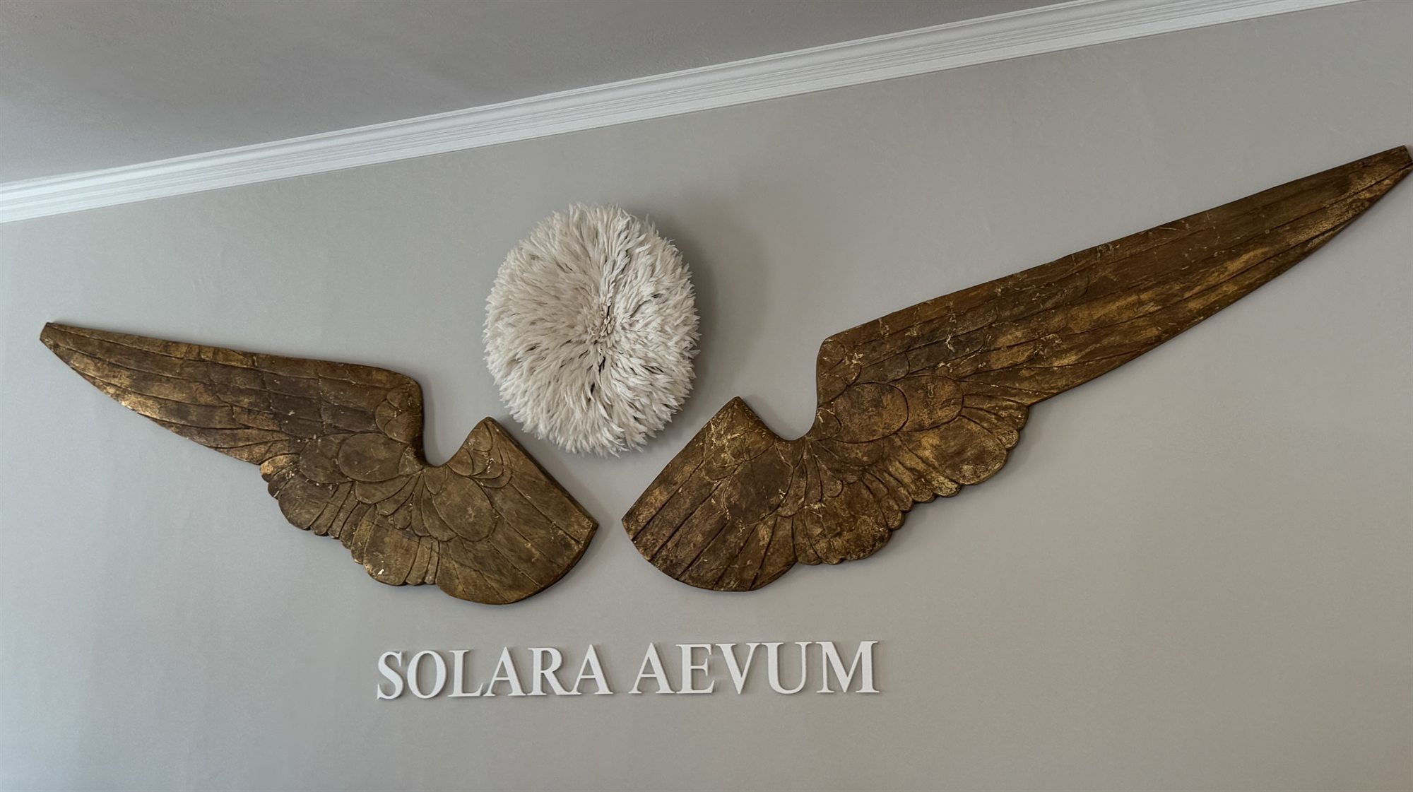 The gilded angel wings and Solara Aevum emblem in the sanctuary — a symbol of light everlasting